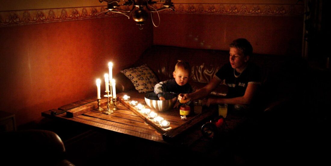 En kvinne og et barn sitter ved et stuebord med mange tente talglys foran seg