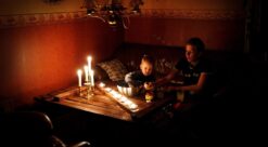 En kvinne og et barn sitter ved et stuebord med mange tente talglys foran seg