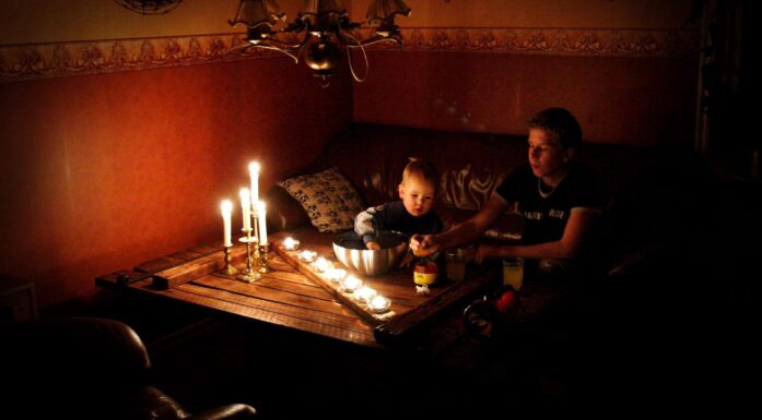 En kvinne og et barn sitter ved et stuebord med mange tente talglys foran seg