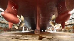 Stort skip ligger i tørrdokk. Bildet er tatt bakfra ved skipets akterende og fokuserer på to propeller - en på hver side av skroget.