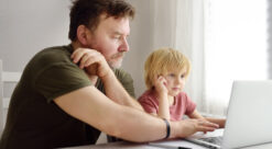 Mann og liten gutt foran pc-skjerm. Til sak om tidlig testi ng av barn i skolen.