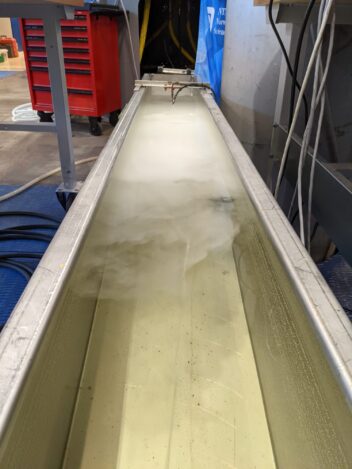 Bilde fra en mekanisk lab. Viser en kunstig elv med melkefarget vann. 