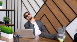 mann med solbriller som sitter med pc og beina på pulten