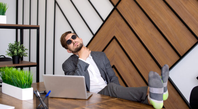 mann med solbriller som sitter med pc og beina på pulten