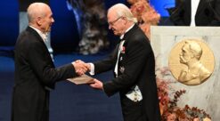 Mann i kjole og hvitt får diplom av Sveriges kong Carl Gustaf