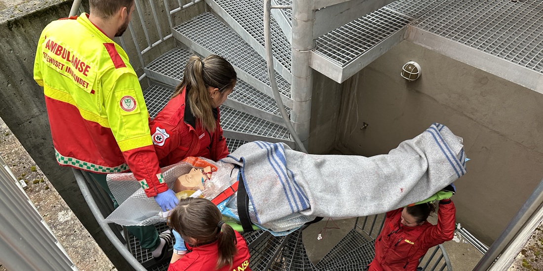 Teamarbeid. Bildet viser en gruppe studenter som bærer en båre opp en vindeltrapp..