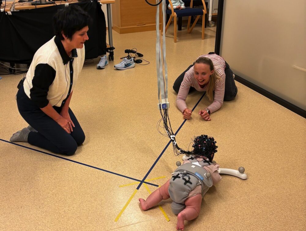 Bildet viser babyen på gulvet med mamma og forsker rundt