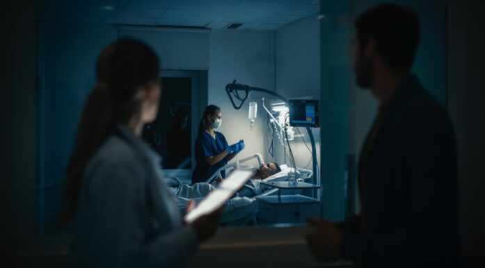 Pasient i sykeseng som passes på av sykepleier og leger. Mørkt rom. Bilde til sak om helsepersonell og rusbruk