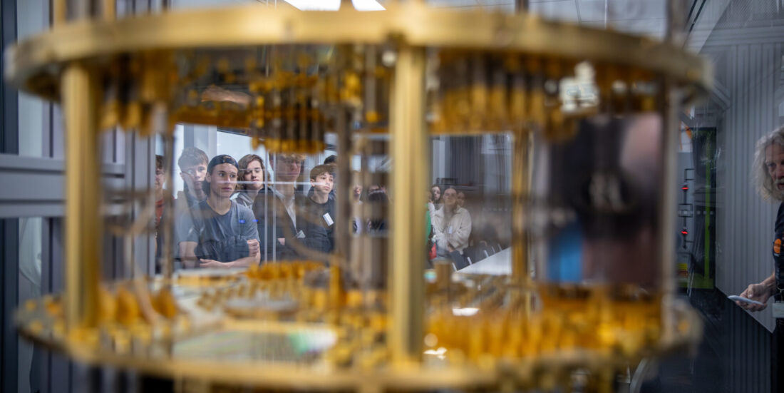 Gløtt inn i superdatamaskin, gullaktige komponenter i forgrunnen, studenter i bakgrunnen