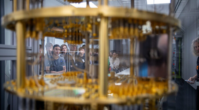 Gløtt inn i superdatamaskin, gullaktige komponenter i forgrunnen, studenter i bakgrunnen