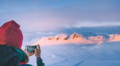 Bildet viser en kvinne med mobiltelefon foran en fjellkjede.