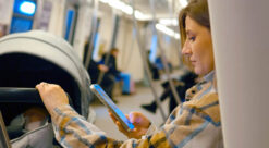 KI. En kvinne på toget scroller på mobilen mens barnevognen står ved siden av henne.