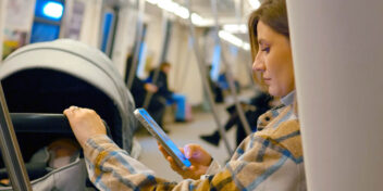 KI. En kvinne på toget scroller på mobilen mens barnevognen står ved siden av henne.