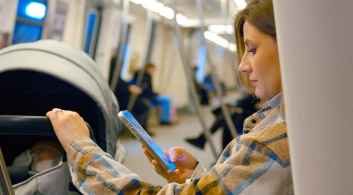 KI. En kvinne på toget scroller på mobilen mens barnevognen står ved siden av henne.