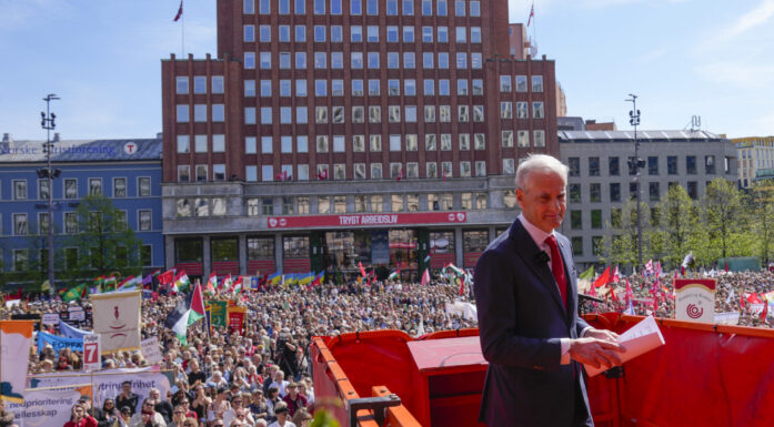 Mann på talerstol foran folkemengde 1. mai. Blå himmel