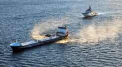 Lasteskip seiler, fulgt av grått kystvaktskip.