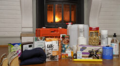 Vannkanner, fyrstikkeksker, primus og mye annet utstyr som inngår i egenberedskap, står på et stuegulv foran en peis som brenner.