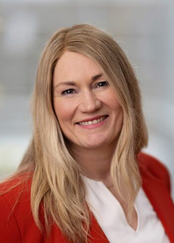 Portrett av kvinne med langt blondt hår, rød jakke. Gra bakgrunn. Til artikkel om arbeid.