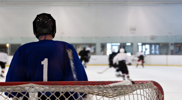 Smerter. En ishockeykeeper sett bakfra betrakter flere spillere ute på isen.