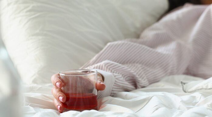 Kvinne ligger i senga med et glass ved siden av seg.