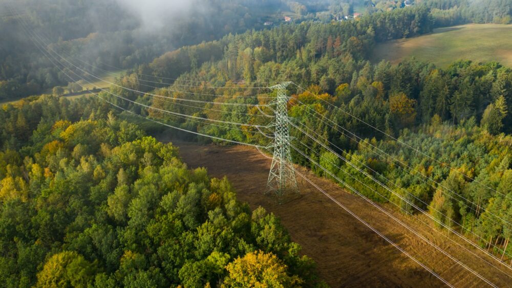 Luftfoto av høyspentledninger og høyspent elektrisk overføring på terrenget omgitt av trær i sollys