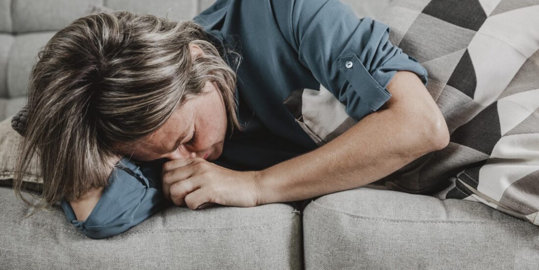Migrene. Foto viser kvinne på sofa med tydelige uttrykk for smerter.