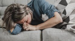 Migrene. Foto viser kvinne på sofa med tydelige uttrykk for smerter.