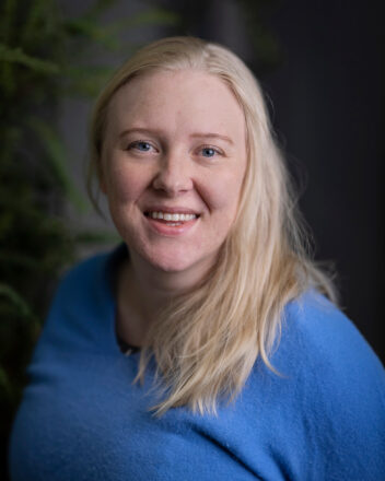 Smilende kvinne med blondt hår og blå genser. Foto.