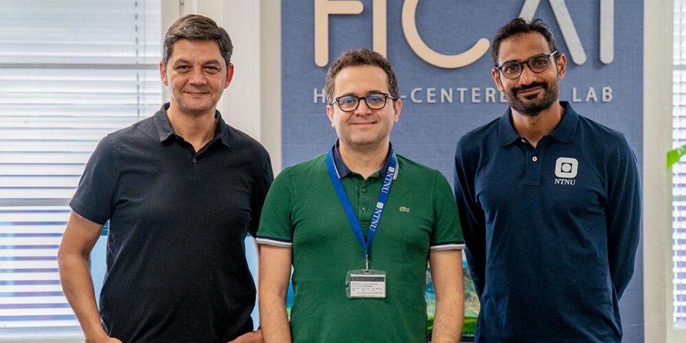 Tre forskere; Eleftherios Papachristos, Yavuz Inal og Sujay Shalawadi står foran en vegg og smiler til kamera. Foto.