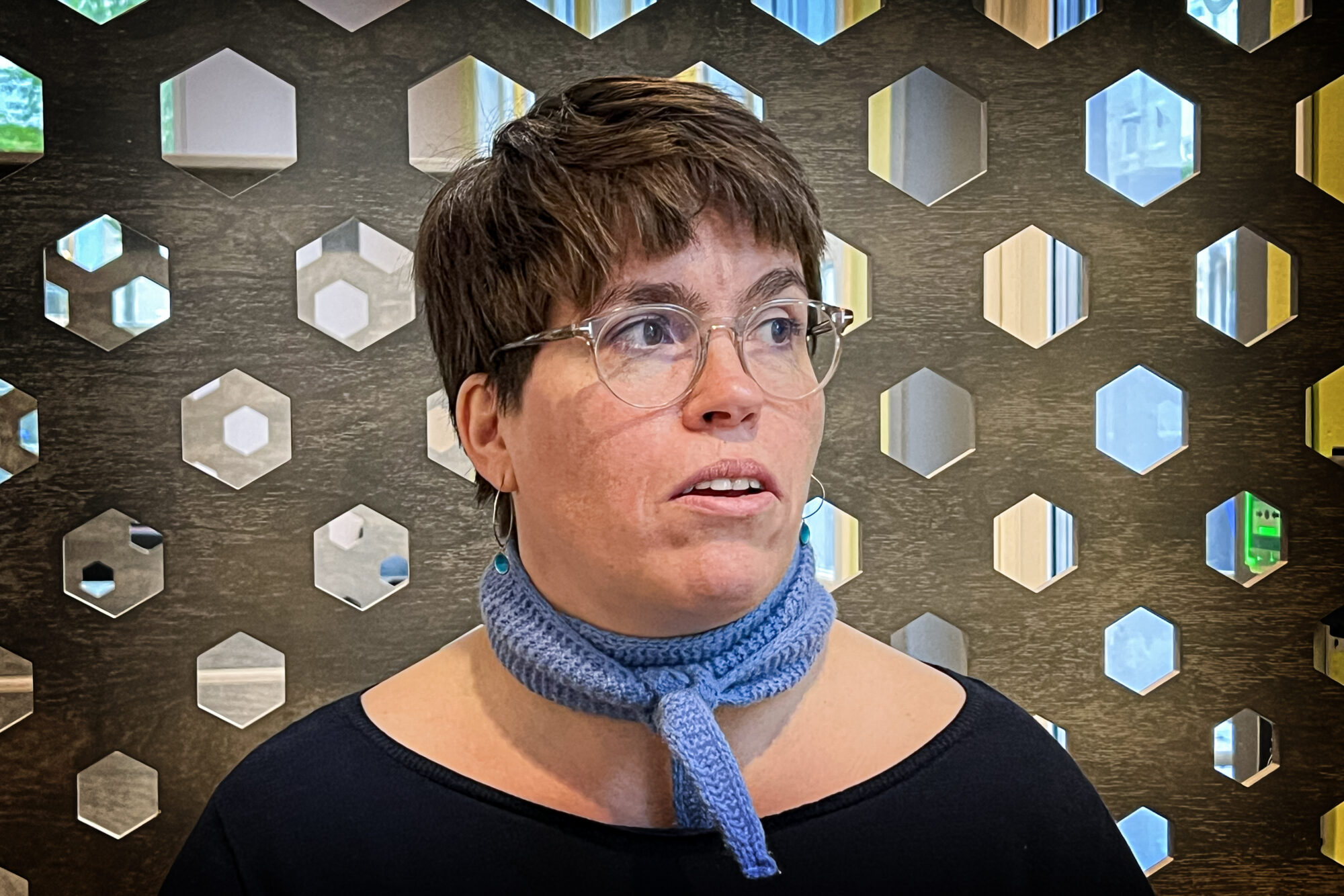 Kvinne med mørkt kort hår mot en grå vegg. Foto.